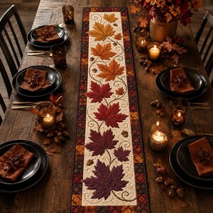 May include: A rectangular table runner featuring a cream-colored center panel with an embroidered pattern of autumn maple leaves in shades of yellow, orange, red, and purple, bordered by a dark plaid fabric with small acorn motifs.