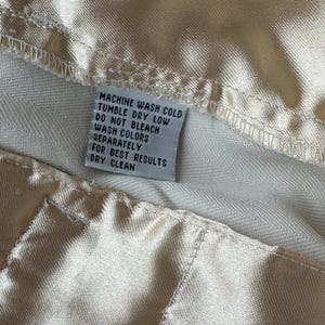 Puede incluir: Primer plano de una tela color crema con una costura y una etiqueta de cuidado. La etiqueta dice: LAVAR A M&Aacute;QUINA EN FR&Iacute;O, SECAR EN SECADORA A BAJA TEMPERATURA, NO USAR LEJ&Iacute;A, LAVAR LOS COLORES POR SEPARADO, PARA OBTENER LOS MEJORES RESULTADOS, LIMPIEZA EN SECO.