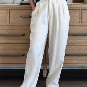 Puede incluir: Pantalones color crema de cintura alta con frente plisado y corte holgado. Los pantalones se combinan con una blusa azul marino y tacones de punta color crema. El atuendo est&aacute; dise&ntilde;ado de manera informal pero elegante.