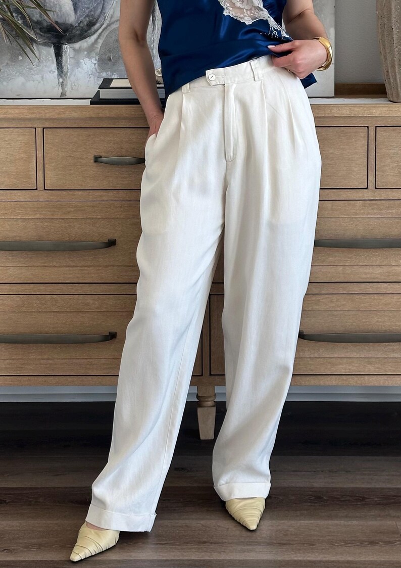 Puede incluir: Pantalones color crema de cintura alta con frente plisado y corte holgado. Los pantalones se combinan con una blusa azul marino y tacones de punta color crema. El atuendo est&aacute; dise&ntilde;ado de manera informal pero elegante.