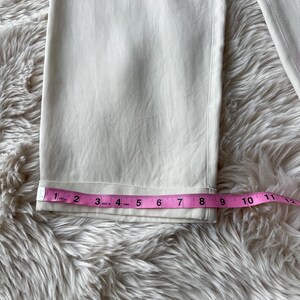 Puede incluir: Primer plano de un pantal&oacute;n color crema con dobladillo doblado. Una cinta m&eacute;trica rosa muestra que el dobladillo mide aproximadamente 20 cm de ancho. El pantal&oacute;n est&aacute; sobre una superficie suave y clara.