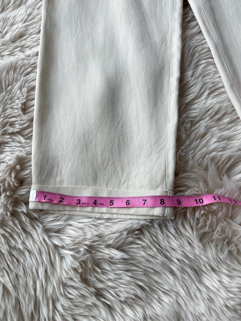 Puede incluir: Primer plano de un pantal&oacute;n color crema con dobladillo doblado. Una cinta m&eacute;trica rosa muestra que el dobladillo mide aproximadamente 20 cm de ancho. El pantal&oacute;n est&aacute; sobre una superficie suave y clara.