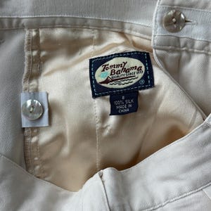 Puede incluir: Primer plano de un pantal&oacute;n de seda color crema con cierre de bot&oacute;n. La etiqueta Tommy Bahama es visible, junto con una etiqueta de talla 8. El pantal&oacute;n est&aacute; hecho de 100% seda.