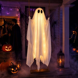 May include: A hanging ghost decoration made of white fabric with two black oval eyes, illuminated from within by warm lights. The ghost is suspended by ropes from a wooden plank base, creating a glowing, spectral figure for Halloween decor.