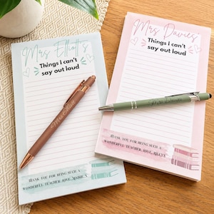 May include: Two rectangular lined notepads with personalised text. The left pad is light blue with 'Mrs Elliott's Things I can't say out loud' and a matching pen. The right pad is light pink with 'Mrs Davies' Things I can't say out loud' and a green pen.