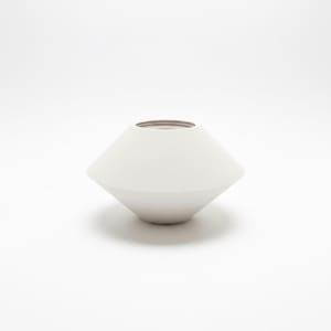 Könnte beinhalten: Eine weiße, geometrische Vase mit einem breiten, abgewinkelten Körper und einer schmalen Öffnung. Die Vase hat eine glatte, matte Oberfläche und eine neutrale Farbpalette, passend für verschiedene Einrichtungsstile. Die Vase ist etwa 15 cm hoch.
