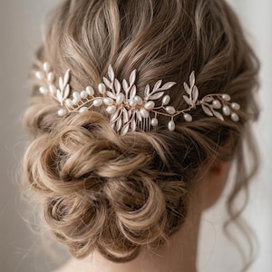 Könnte beinhalten: Ein zarter Brauthaarkamm mit floralem und Blätterdesign. Der goldfarbene Metallkamm ist mit Kunstperlen und Blättern verziert. Das Haaraccessoire ist für das Tragen im Haar für eine Hochzeit oder einen besonderen Anlass konzipiert.