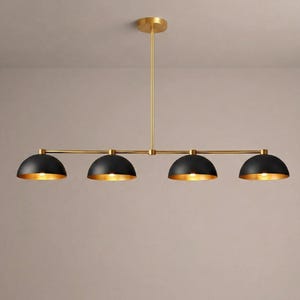 Può includere: Una moderna lampada a sospensione a quattro luci. L'apparecchio presenta quattro paralumi neri a forma di cupola con interni dorati, sospesi a un telaio in metallo dorato. La lampada è progettata per il montaggio a soffitto e aggiunge un tocco di stile contemporaneo.