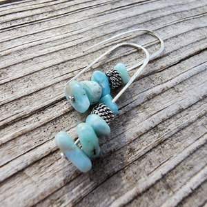 May include: A pair of silver dangle earrings with light blue gemstone beads. The earrings are made with a silver wire and have a simple design.