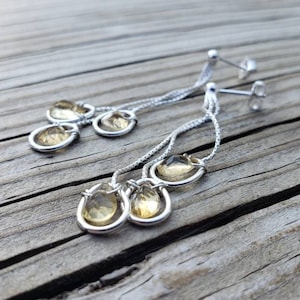 May include: Silver dangle earrings with three teardrop-shaped yellow gemstones.