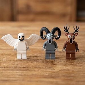 Op de afbeelding: Drie Lego dierenfiguren: een witte uil met vleugels, een grijze ram en een bruin hert. De uil heeft een zwarte snavel en ogen. De ram heeft grote zwarte hoorns. Het hert heeft geweien en een open mond. Op een houten oppervlak.