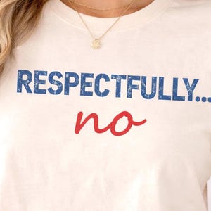 May include: Cream-colored t-shirt with the text "RESPECTFULLY... no" in blue and red. The shirt has a classic crew neck and short sleeves. The text is centered on the front of the shirt.