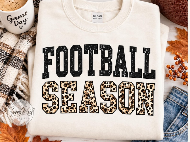 May include: A cream-colored crewneck sweatshirt featuring the text FOOTBALL SEASON in a bold, block-letter font. The word FOOTBALL is printed in a distressed black texture, while the word SEASON features a brown and black leopard print pattern.