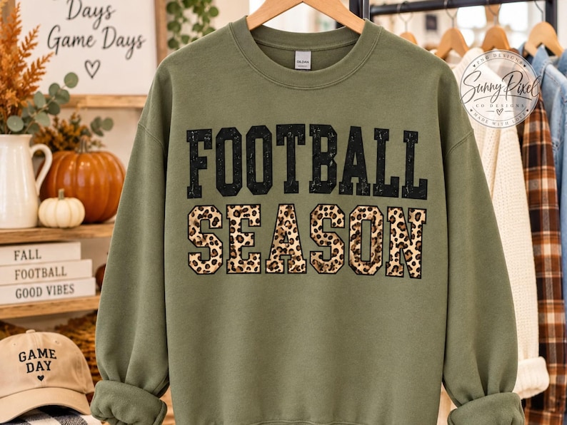 May include: An olive green crewneck sweatshirt featuring the text FOOTBALL SEASON in a bold, block-letter font. The word FOOTBALL is printed in solid black, while the word SEASON is filled with a brown and black leopard print pattern.