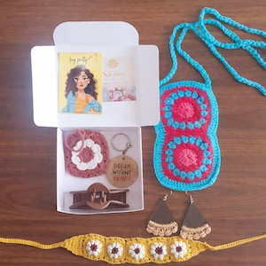 Könnte beinhalten: Eine Sammlung handgefertigter Accessoires, darunter eine Häkeltasche, Ohrringe und ein Stirnband mit Gänseblümchen-Akzenten. Eine Box enthält einen Häkeluntersetzer, eine Haarspange und einen Schlüsselanhänger mit dem Text "Dream Without Fear".