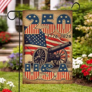 Puede incluir: Una bandera de jardín con un diseño patriótico. La bandera presenta el número "250" en rojo, blanco y azul, junto con el texto "1776-2026" y "USA". También se representa una bandera estadounidense y un cañón. La bandera se muestra en un soporte de metal negro.