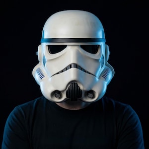 May include: A white Stormtrooper helmet with black accents and dark visor. The helmet has a distinctive design with a rounded top, a black band, and detailed facial features. The helmet is a Star Wars collectible.