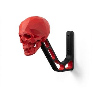 Puede incluir: Una calavera roja geométrica montada en un gancho de pared negro y rojo. La calavera es un diseño tridimensional detallado. El gancho tiene una forma curva con una placa de montaje.
