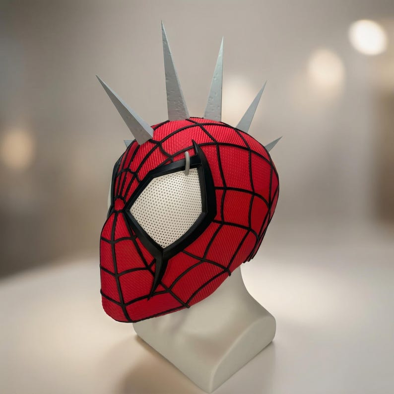 May include: A red and black Spider-Man mask with a web pattern, black trim, and white mesh eye coverings. The mask has silver spikes protruding from the top. The mask is displayed on a white mannequin head.