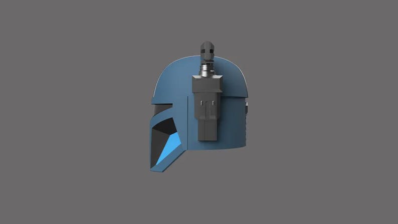 Puede incluir: Un casco azul mandaloriano con un accesorio lateral y un fondo gris oscuro. El casco tiene una forma distintiva con rasgos angulares y un &aacute;rea de visor con un acento azul.