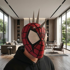May include: A red and black Spider-Man mask with a unique design featuring silver spikes on the head. The mask has a web pattern and large eye openings with a mesh material. The person is wearing a black hoodie.