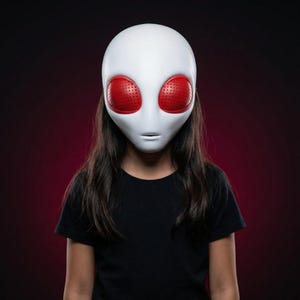 Puede incluir: Una máscara de alienígena blanca con grandes ojos rojos. La máscara tiene una superficie lisa. La persona que lleva la máscara lleva una camiseta negra. El fondo es un degradado rojo oscuro.
