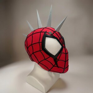 May include: A red and black Spider-Man mask with a web pattern, black eye frames, and white mesh eye coverings. The mask has silver spikes attached to the top. The mask is displayed on a white mannequin head.