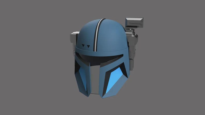 Puede incluir: Casco mandaloriano azul y gris con un dise&ntilde;o distintivo. El casco presenta una franja blanca central, formas geom&eacute;tricas y un dispositivo montado lateralmente. La est&eacute;tica general sugiere un tema futurista de ciencia ficci&oacute;n.