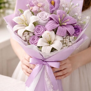 May include: A handcrafted bouquet of crochet flowers in shades of white, lavender, and purple. The bouquet includes lilies, roses, and other floral elements, wrapped in lavender paper and tied with a matching ribbon. A unique, handmade gift.