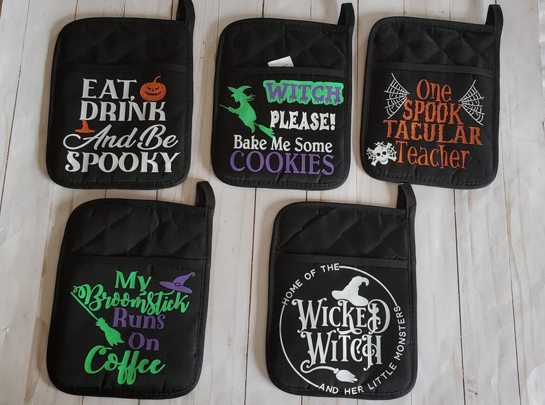 Peut inclure: Ensemble de six maniques matelass&eacute;es noires avec des broderies sur le th&egrave;me d'Halloween. Les motifs comprennent "Eat, Drink and Be Spooky", "Witch Please! Bake Me Some Cookies", "One Spooktacular Teacher", "My Broomstick Runs On Coffee", "Home of the Wicked Witch and Her Little Monsters", et une sorci&egrave;re avec un chaudron.