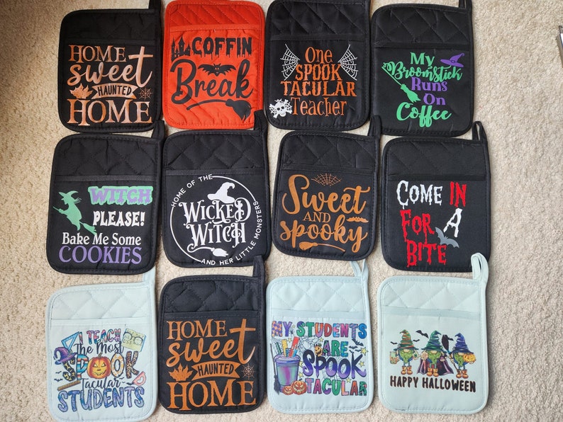 Peut inclure: Ensemble de 10 maniques de cuisine sur le th&egrave;me d'Halloween. Les maniques sont noires, rouges et bleues avec diff&eacute;rents motifs et textes, notamment "Home Sweet Haunted Home", "Coffin Break", "One Spook Tacular Teacher", "My Broomstick Runs On Coffee", "Witch Please! Bake Me Some Cookies", "Home of the Wicked Witch", "Sweet and Spooky", "Come In For A Bite", "I Teach The Most Spook Tacular Students", and "Happy Halloween".
