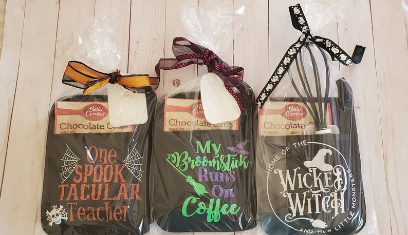 Peut inclure: Trois torchons de cuisine noirs avec des motifs sur le th&egrave;me d'Halloween. La premi&egrave;re serviette a une toile d'araign&eacute;e et le texte "One Spooktacular Teacher". La deuxi&egrave;me serviette a un balai et le texte "My Broomstick Runs On Coffee". La troisi&egrave;me serviette a un chapeau de sorci&egrave;re et le texte "Home of the Wicked Witch and Her Little Monsters".