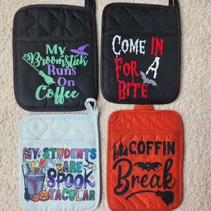 Peut inclure: Quatre maniques de cuisine sur le th&egrave;me d'Halloween. La premi&egrave;re est noire avec le texte "My Broomstick Runs On Coffee" en vert et violet. La deuxi&egrave;me est noire avec le texte "Come In For A Bite" en rouge et blanc. La troisi&egrave;me est bleu clair avec le texte "My Students Are Spooktacular" en arc-en-ciel. La quatri&egrave;me est orange avec le texte "Coffin Break" en noir.
