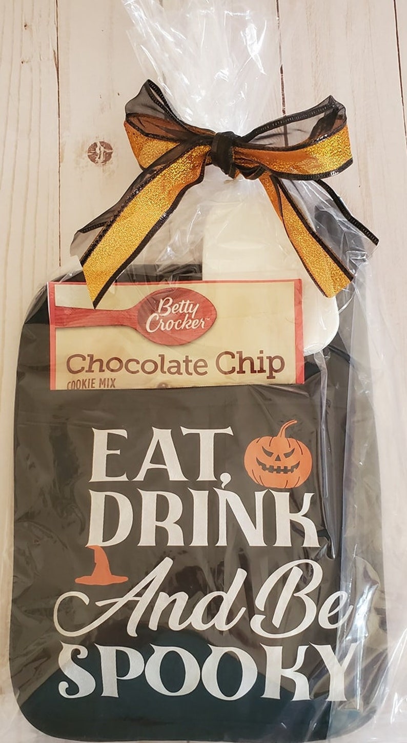 Peut inclure: Un torchon de cuisine noir et blanc sur le th&egrave;me d'Halloween avec le texte "Eat, Drink and Be Spooky" et un graphique de citrouille. Un paquet de m&eacute;lange &agrave; biscuits aux p&eacute;pites de chocolat Betty Crocker est inclus dans le sac cadeau.