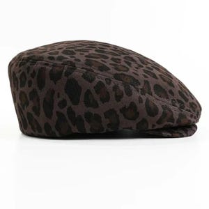 May include: A brown flat cap with a leopard print pattern. The cap is made of a textured fabric and features a classic design. This hat is a stylish accessory for various outfits.