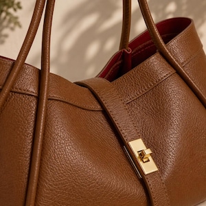 Soft pink leather tote purse for women with elegant gold closure and minimalist aesthetic styling.