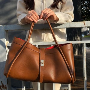 Minimalist black leather shoulder tote bag with structured silhouette and premium pebbled calf leather texture.
