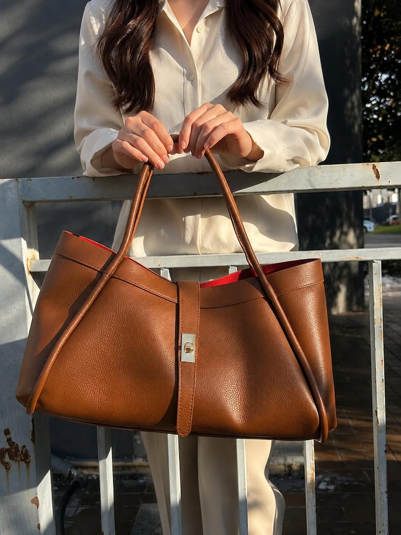 Minimalist black leather shoulder tote bag with structured silhouette and premium pebbled calf leather texture.