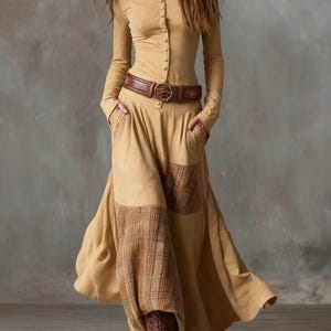 May include: A long-sleeved, button-down dress in a tan color, featuring a brown leather belt with a decorative buckle. The dress has a flowing skirt with plaid patches and is paired with brown boots.