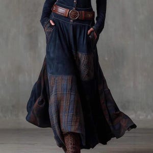 May include: A long, dark blue denim skirt with plaid patches and a brown leather belt. The skirt has a flowing design with pockets and a button-up front. The belt features a large, decorative buckle.