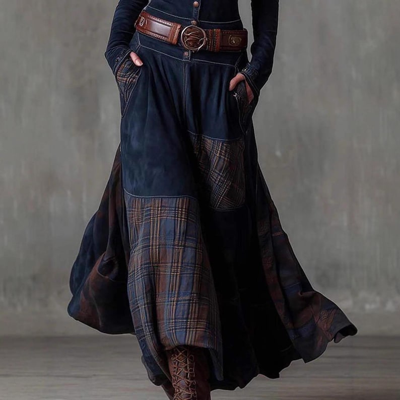 May include: A long, dark blue denim skirt with plaid patches and a brown leather belt. The skirt has a flowing design with pockets and a button-up front. The belt features a large, decorative buckle.