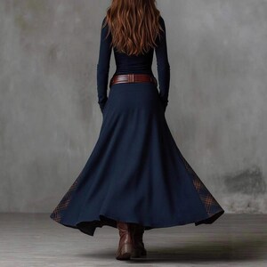 May include: A long-sleeved navy blue dress with a brown belt and a flowing skirt. The skirt has a plaid pattern detail at the hem. The model is wearing brown boots. The dress is suitable for fall or winter wear.