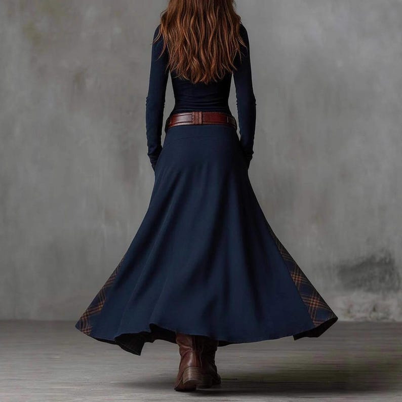 May include: A long-sleeved navy blue dress with a brown belt and a flowing skirt. The skirt has a plaid pattern detail at the hem. The model is wearing brown boots. The dress is suitable for fall or winter wear.
