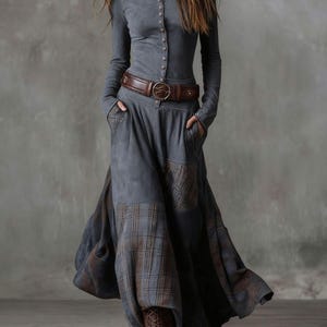 May include: A long-sleeved gray dress with a button-up front and a brown leather belt. The dress features a flowing skirt with plaid patches and is paired with brown lace-up boots. The overall style is bohemian.
