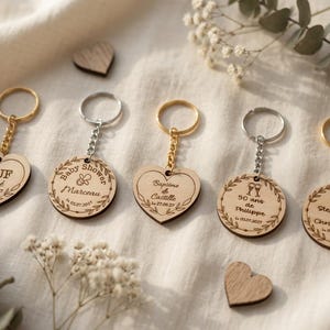 Peut inclure: Cinq porte-clés en bois en forme de cœur et de cercle avec des anneaux et des chaînes en métal. Les gravures incluent des textes tels que EVJF Chloé, Baby Shower Marceau, Baptême de Castille, 50 ans de Philippe et Stephanie & Christophe avec dates.