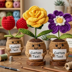 May include: Three crochet flower arrangements with smiling pot-shaped bases. One has a red tulip, another a yellow rose, and the third a purple flower. Each pot holds a sign that reads "Custom Text".