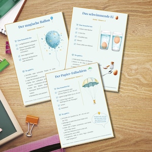 May include: Educational science experiment cards on a wooden surface. The cards feature illustrations and instructions for experiments like a floating egg, a paper parachute, and a magic balloon. The cards have German text.