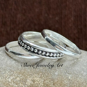 May include: A set of three silver rings stacked together. One ring features a smooth, polished band, another is a plain band, and the center ring displays a detailed beaded texture along its entire circumference. The metal has a bright finish.