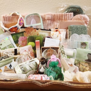 May include: A collection of assorted items including a crocheted floral headband, a clear pouch, a green wallet with floral embossing, a small lantern, a pink floral patterned case, various stationery, skincare products, and decorative accessories.