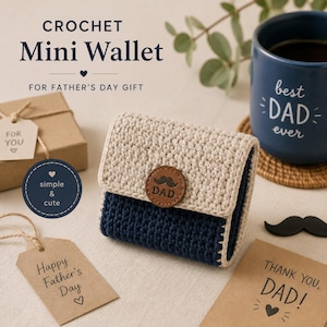Puede incluir: Una mini cartera de ganchillo bicolor con solapa superior beige y base azul oscuro, asegurada con un botón circular de cuero marrón grabado con un bigote y la palabra DAD. La cartera está rodeada de etiquetas de regalo y una taza azul.